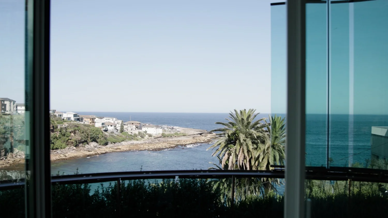 Coastal view from a window, showing palm trees, houses, and ocean.