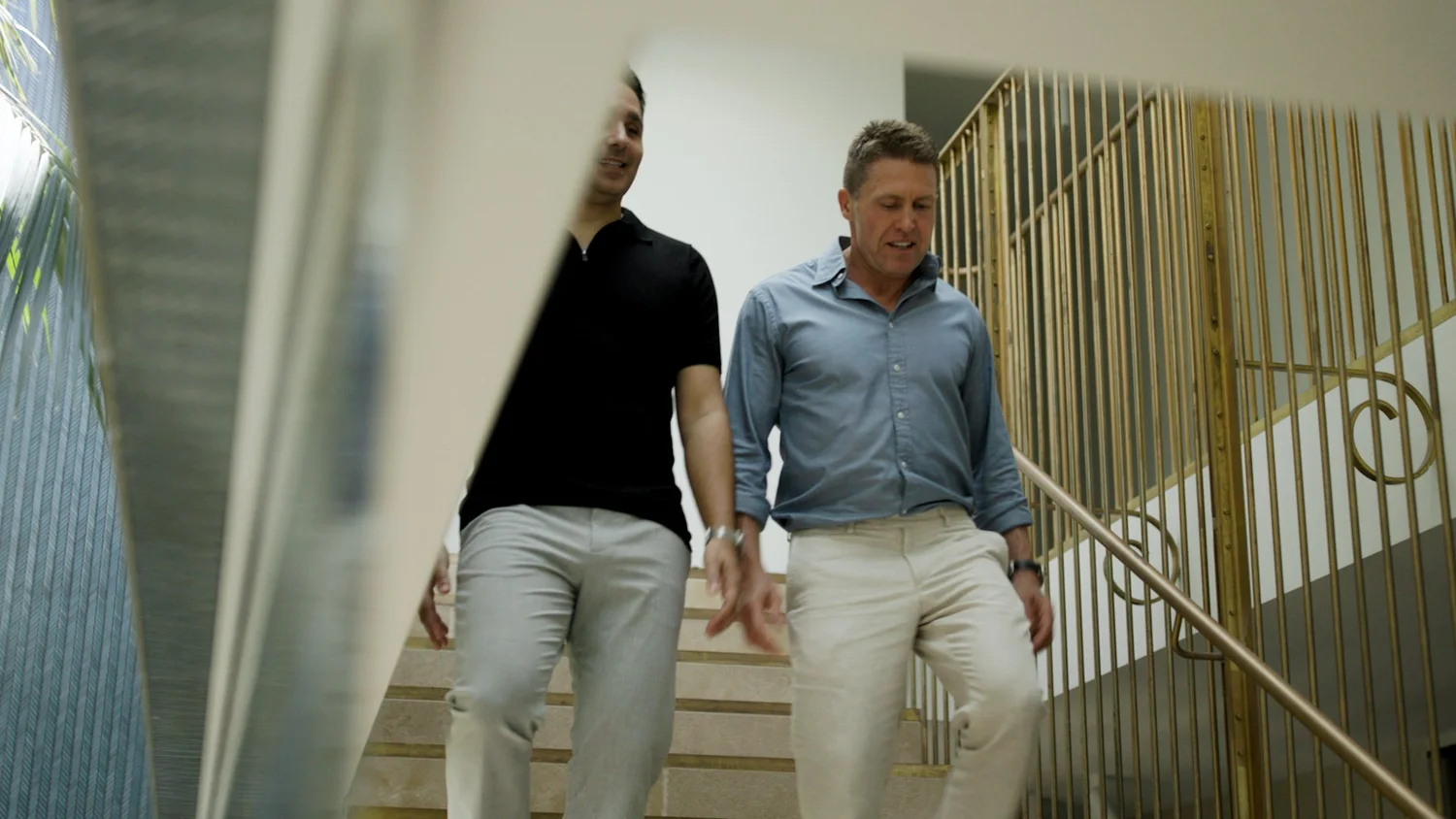 Providence Property Directors, Jay Pace and Lynton Stevenson, walking down a staircase with a gold-colored railing indoors.