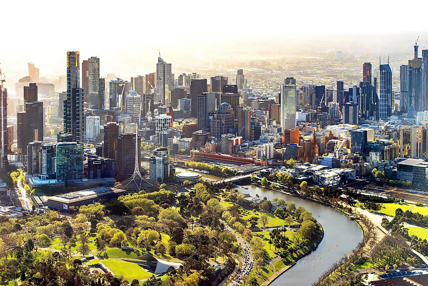 Aerial view of Melbourne cityscape with skyscrapers and Yarra River, featuring lush parks and greenery.